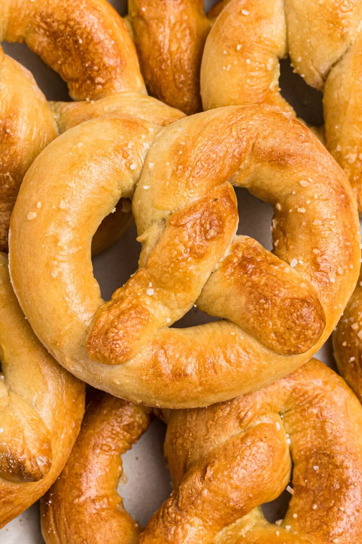 Golden soft pretzels stacked on a white plate and sprinkled with coarse salt. 