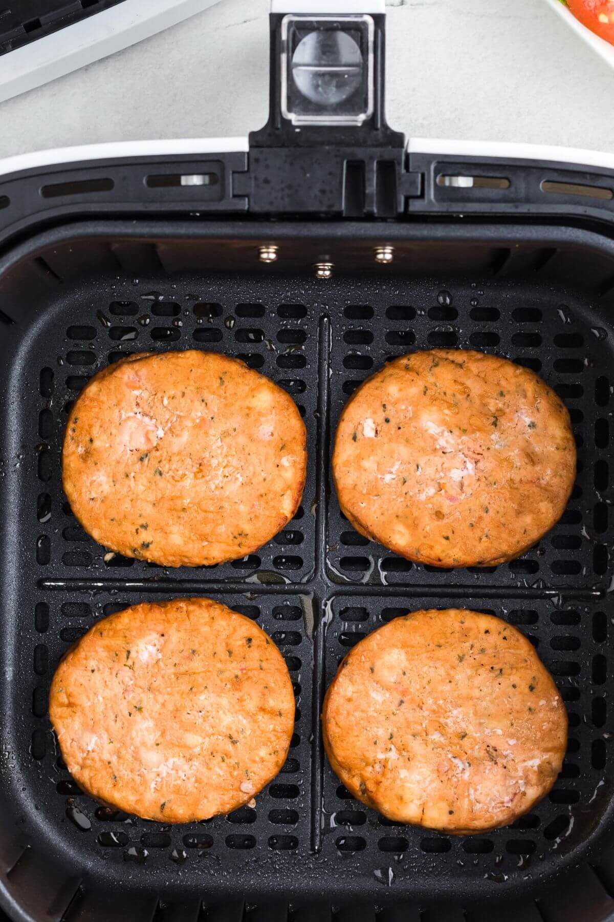 Four pink cooked salmon patties in the air fryer basket. 