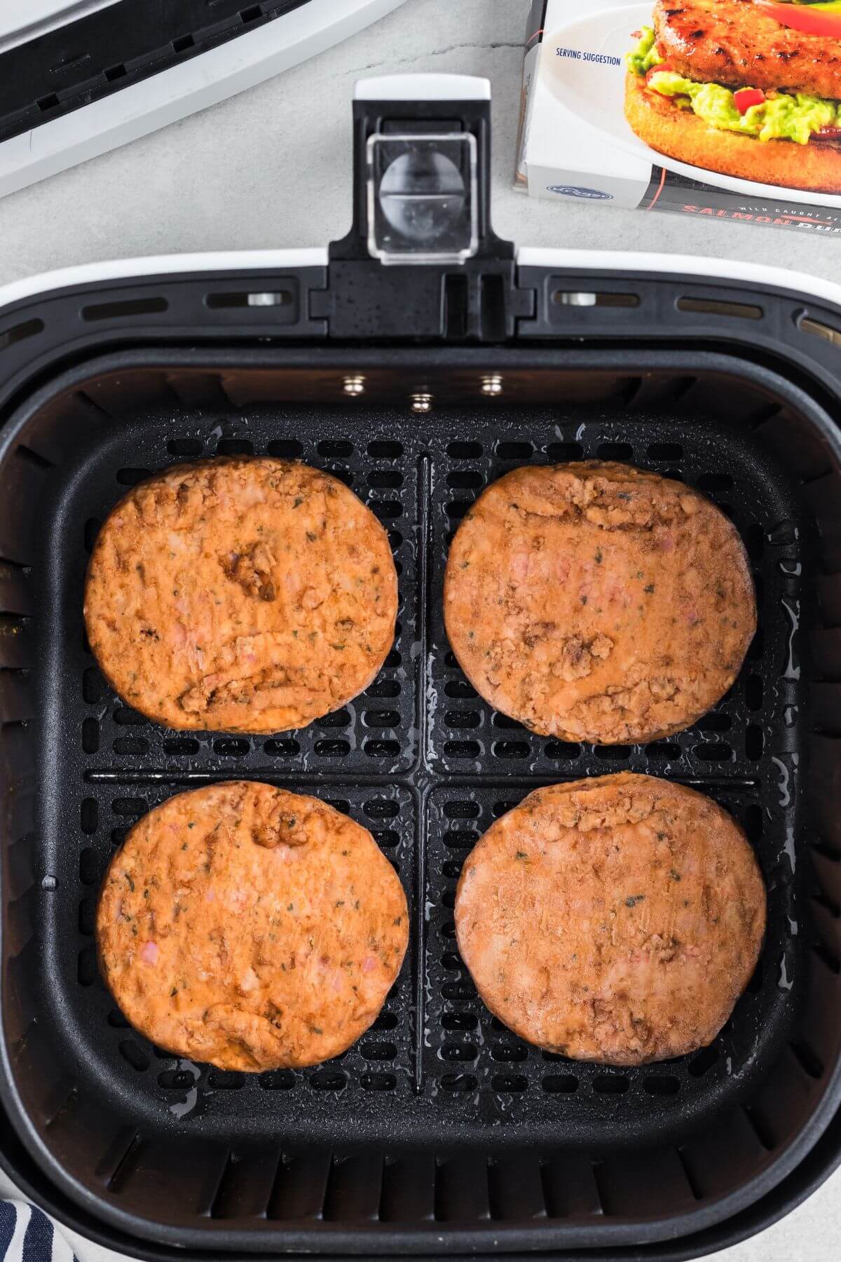 Frozen salmon burgers in the air fryer basket before being cooked. 