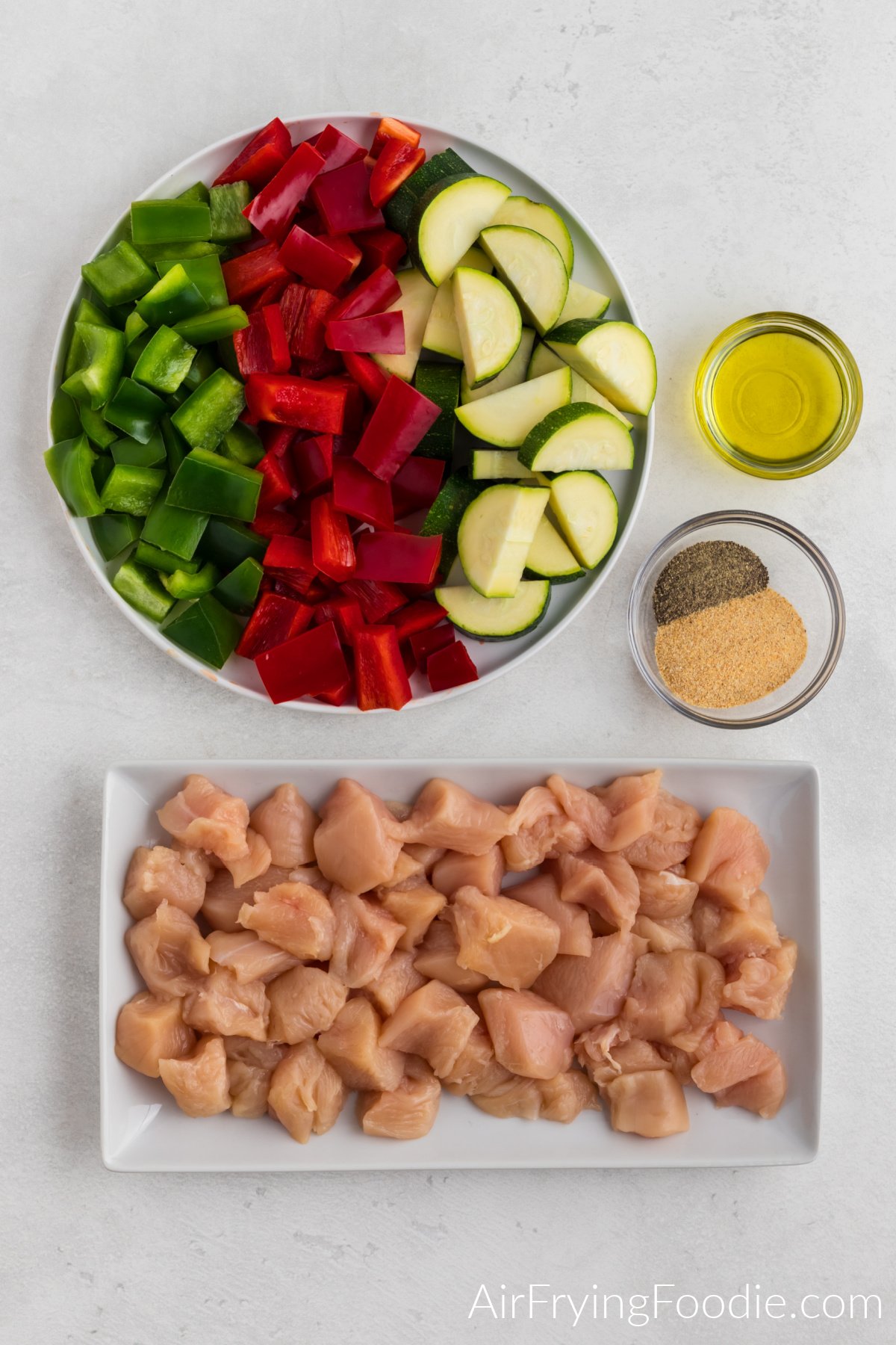 vegetables cut into pieces, olive oil, seasonings, and chicken cut into pieces on a white table.