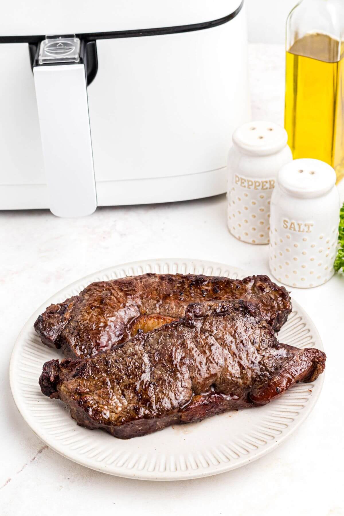Juicy cooked steaks on a white plate in front of the air fryer. 