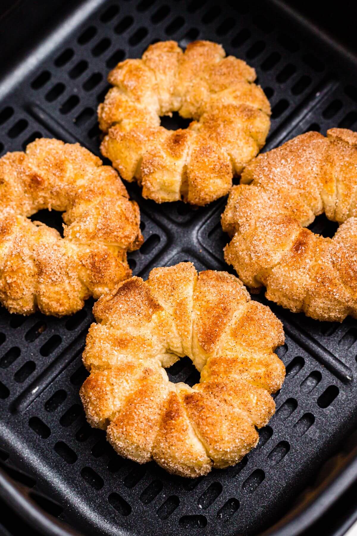 Golden brown puff pastry wrapped apple rings in the air fryer basket after being cooked. 