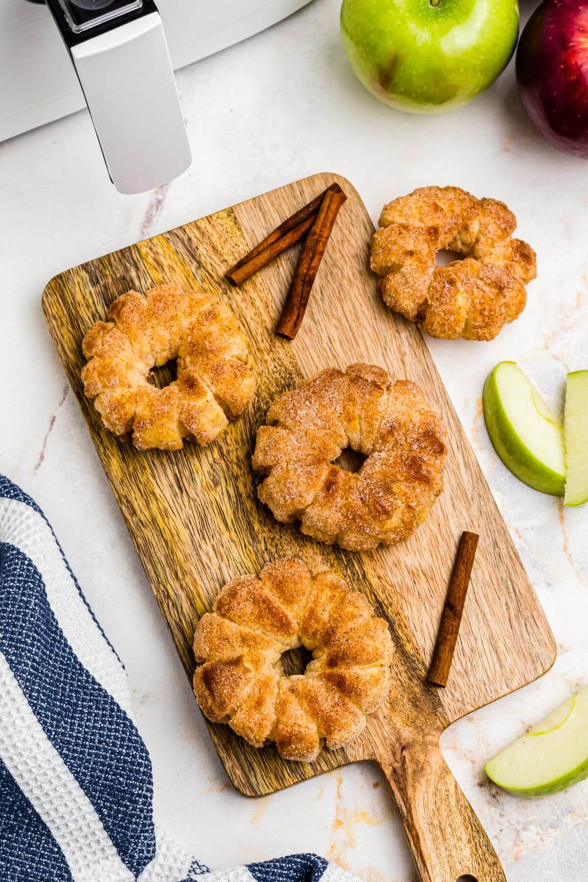 Golden puff pastry wrapped apple rings on a cutting board with apple slices on the table. 