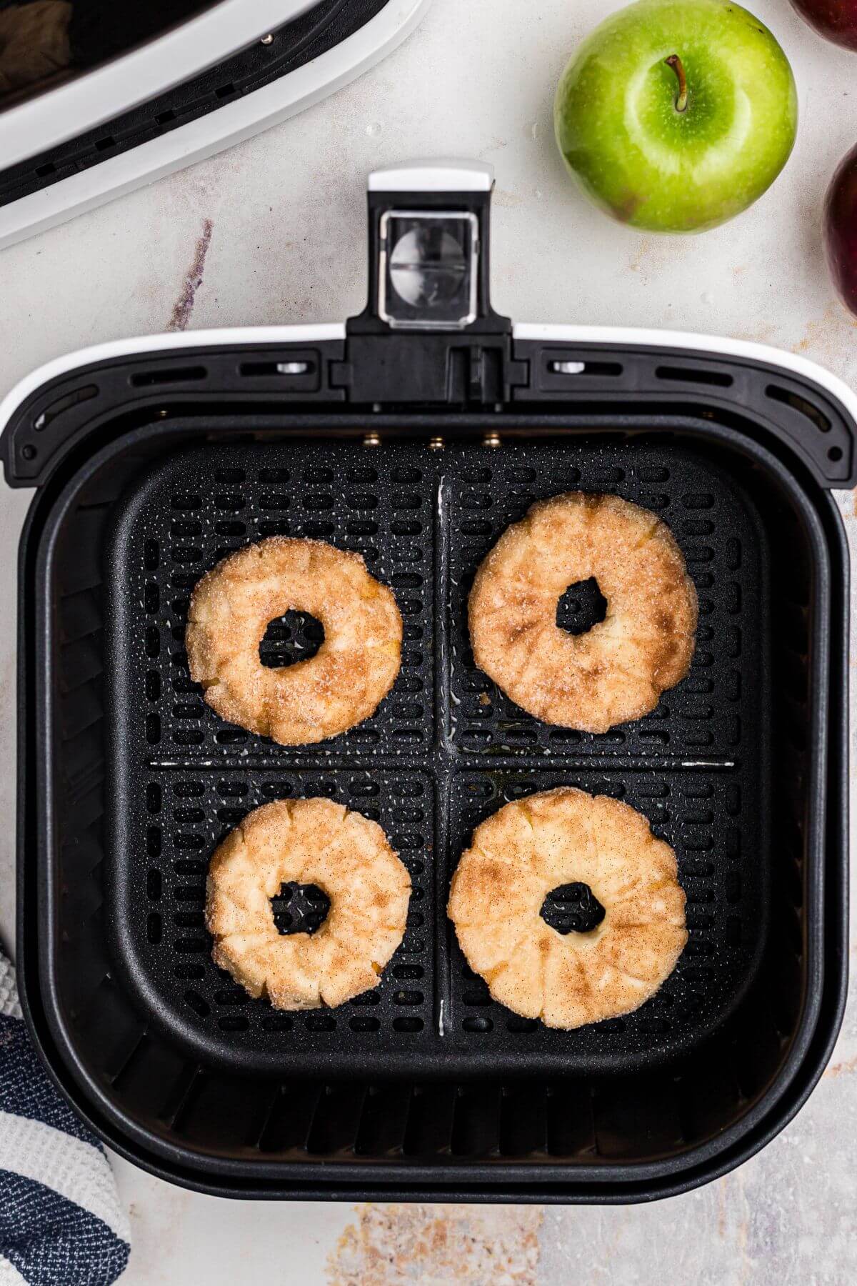 Apple rings wrapped in pastry dough, in the air fryer basket before cooking. 