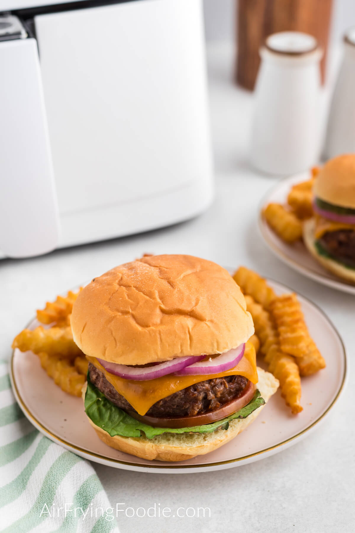 Air fryer Beyond burger dressed with toppings and a bun and served on a plate with a side of fries. 
