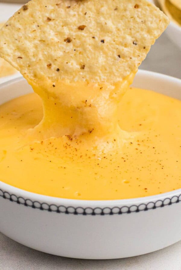 Tortilla chip being dipped into melted cheese in small white bowl.