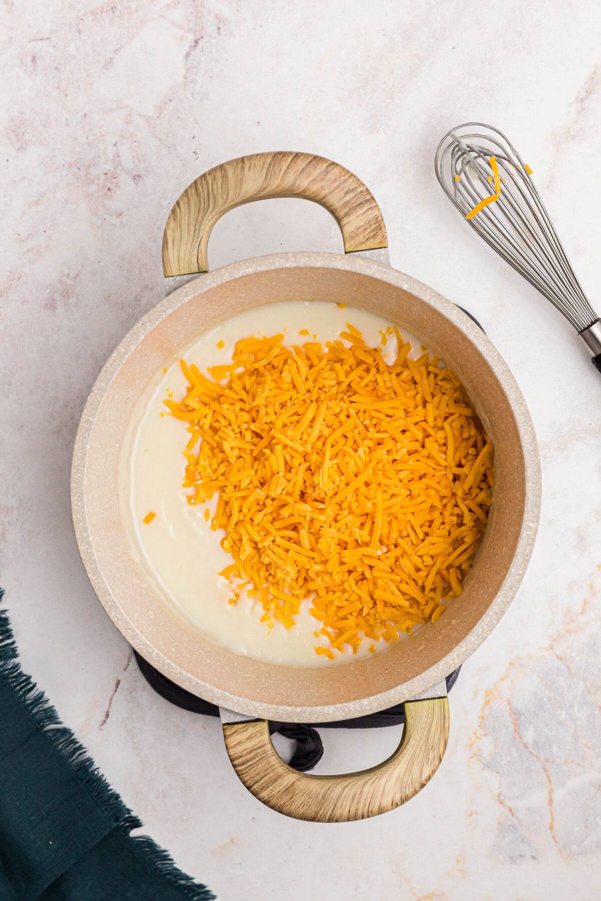 Shredded cheddar cheese being added to the creamy mixture in a sauce pan. 