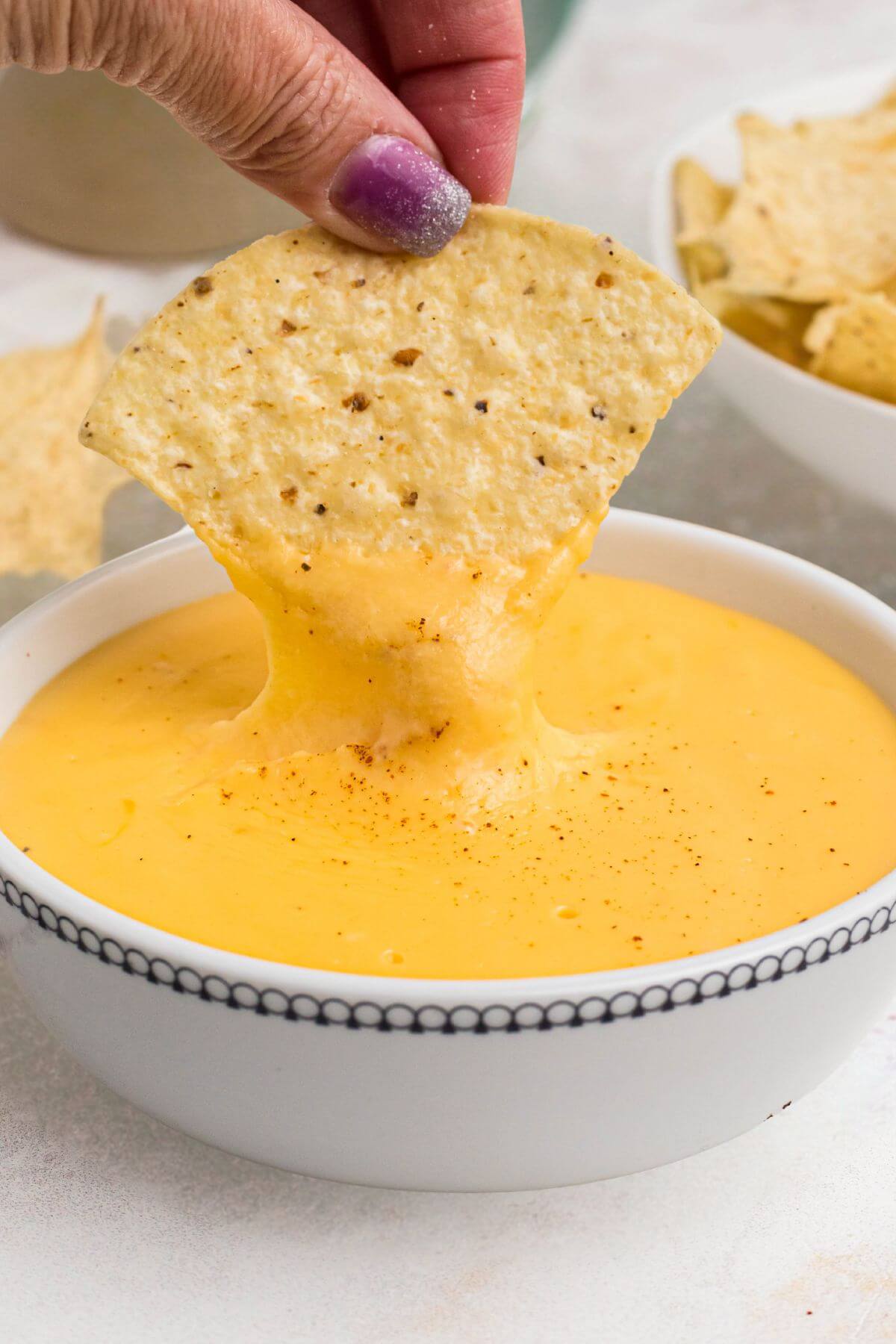 Tortilla chip being dipped into melted cheese in a small white bowl. 