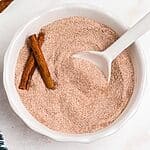 Cinnamon sugar mixed in a white bowl with a small white spoon on a marble table.