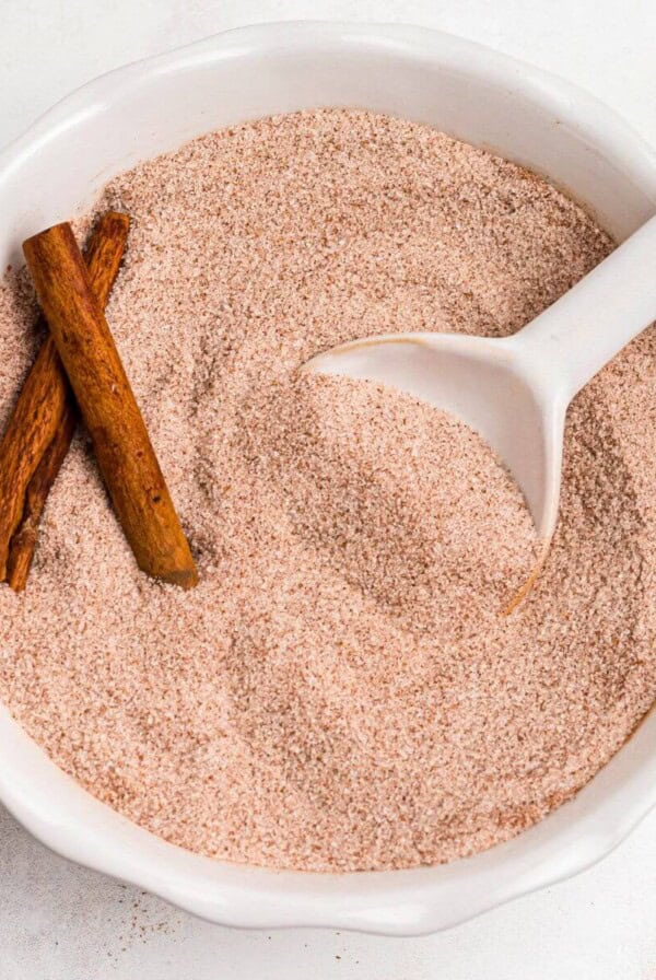 Cinnamon sugar mixed in a white bowl with a small white spoon on a marble table.