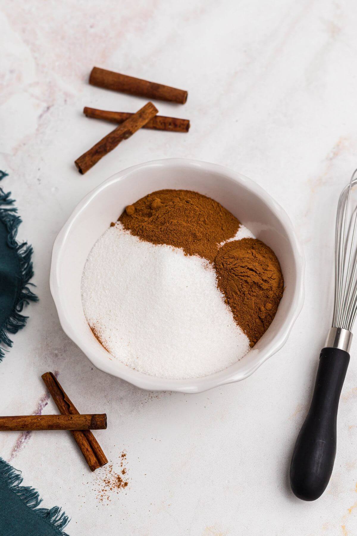 Cinnamon and sugar being mixed together in a small white bowl with a whisk on the table. 