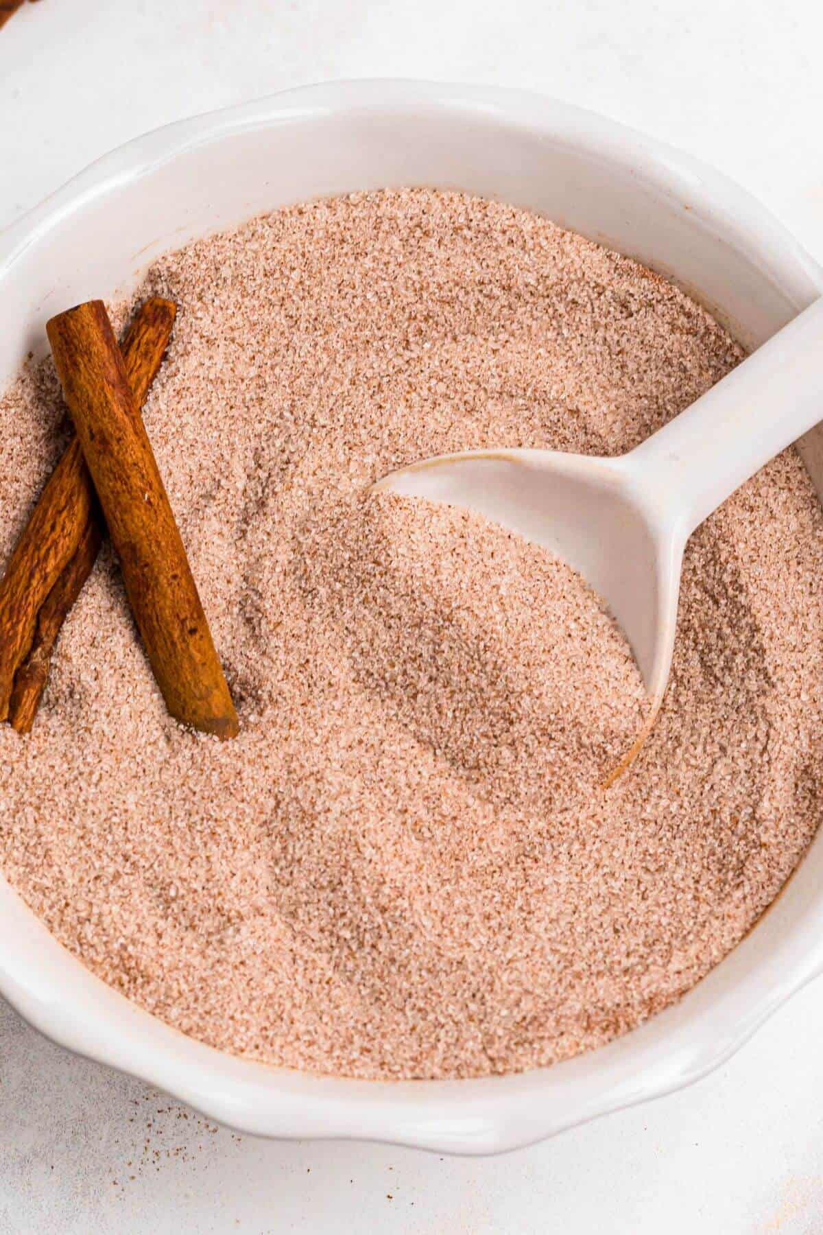 Sugar and cinnamon being mixed together in a white bowl with a white spoon. 