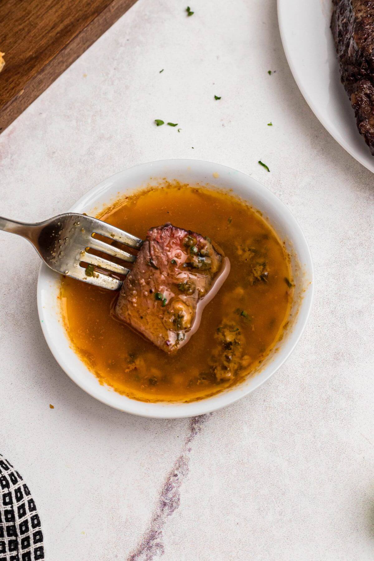 Melted cowboy butter in a white bowl with a piece of steak being dipped in the sauce. 