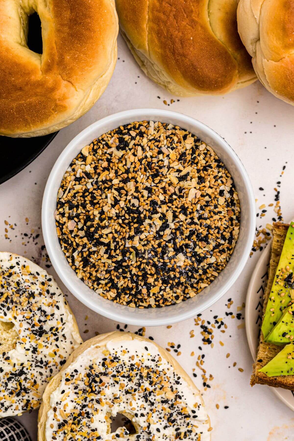 Everything Bagel Seasoning in a small bowl surrounded by bagels and avocado toast. 