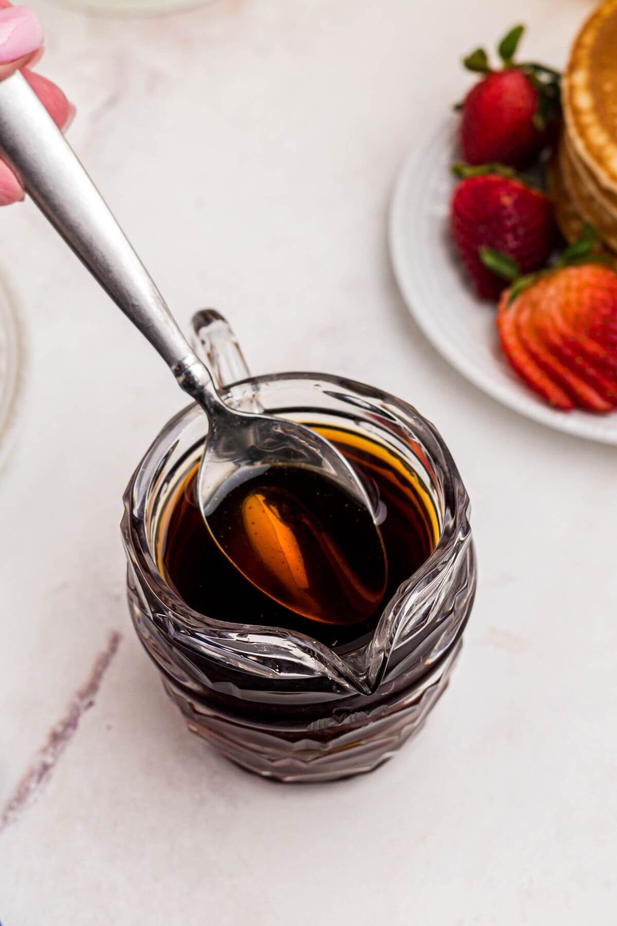 Freshly homemade syrup in a clear glass serving dish with a spoon lifting some syrup out. 