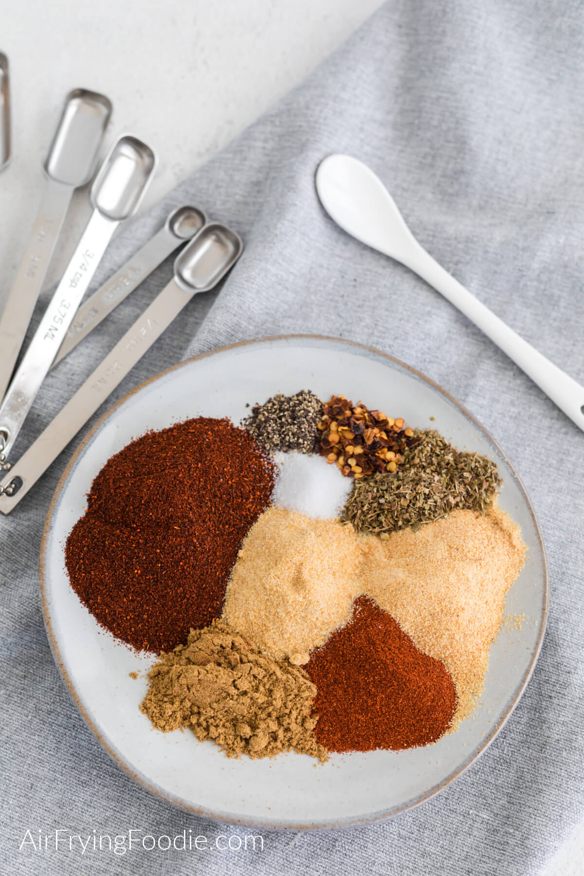 Seasonings needed to make taco seasoning measured out on a plate, ready to be mixed together. 