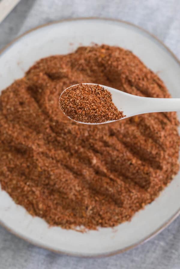 Overhead photo of homemade taco seasoning on a white plate with a spoonful of the seasoning close up.