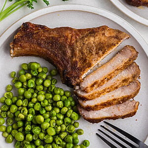 Air fried pork steak sliced and served on a plate with green peas.