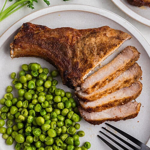 Air fried pork steak sliced and served on a plate with green peas.