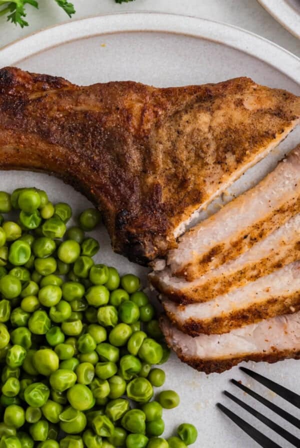 Air fried pork steak sliced and served on a plate with green peas.