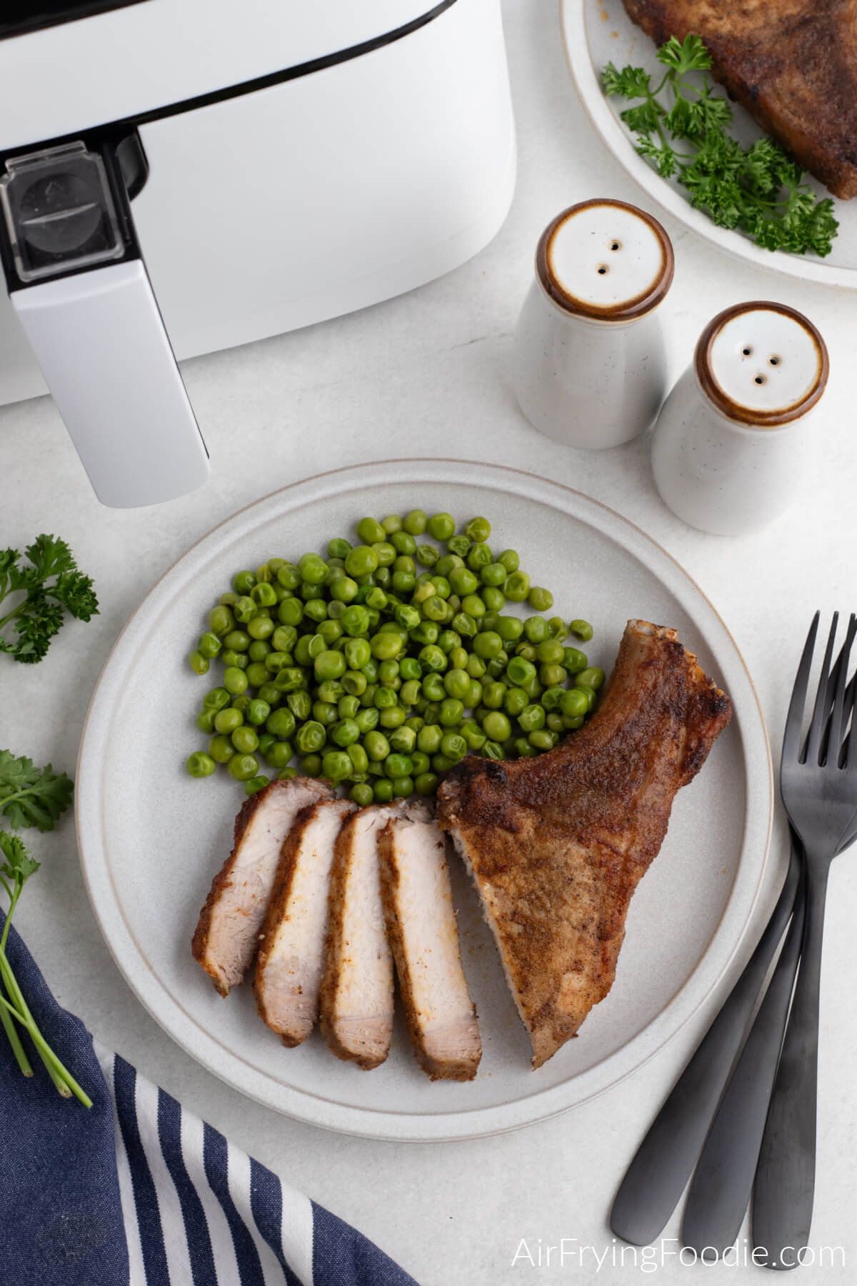 Overhead photo of pork steakmade in the air fryer, sliced and served with green peas. 