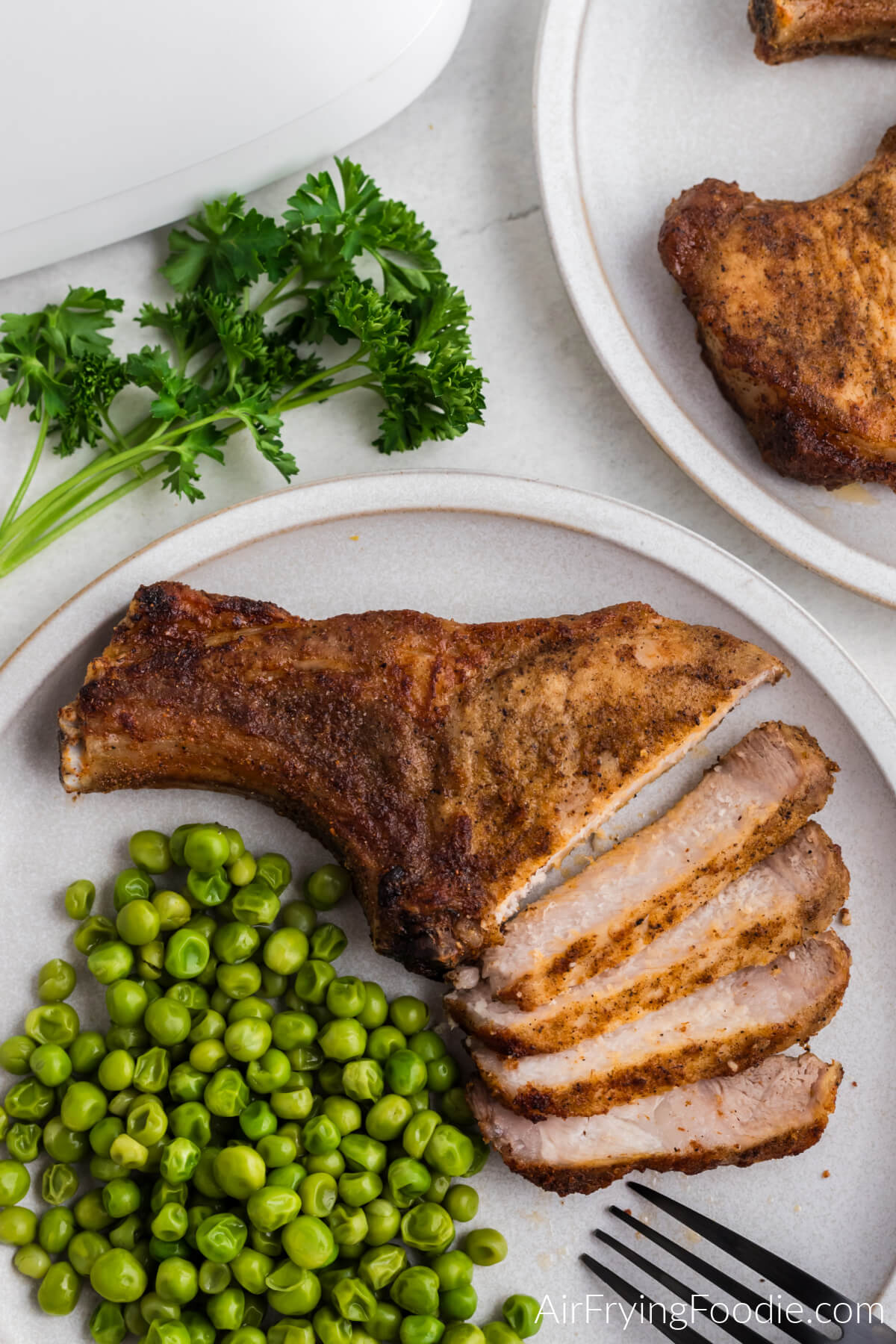Pork steak air fried and sliced on a white plate with a side of green peas.
