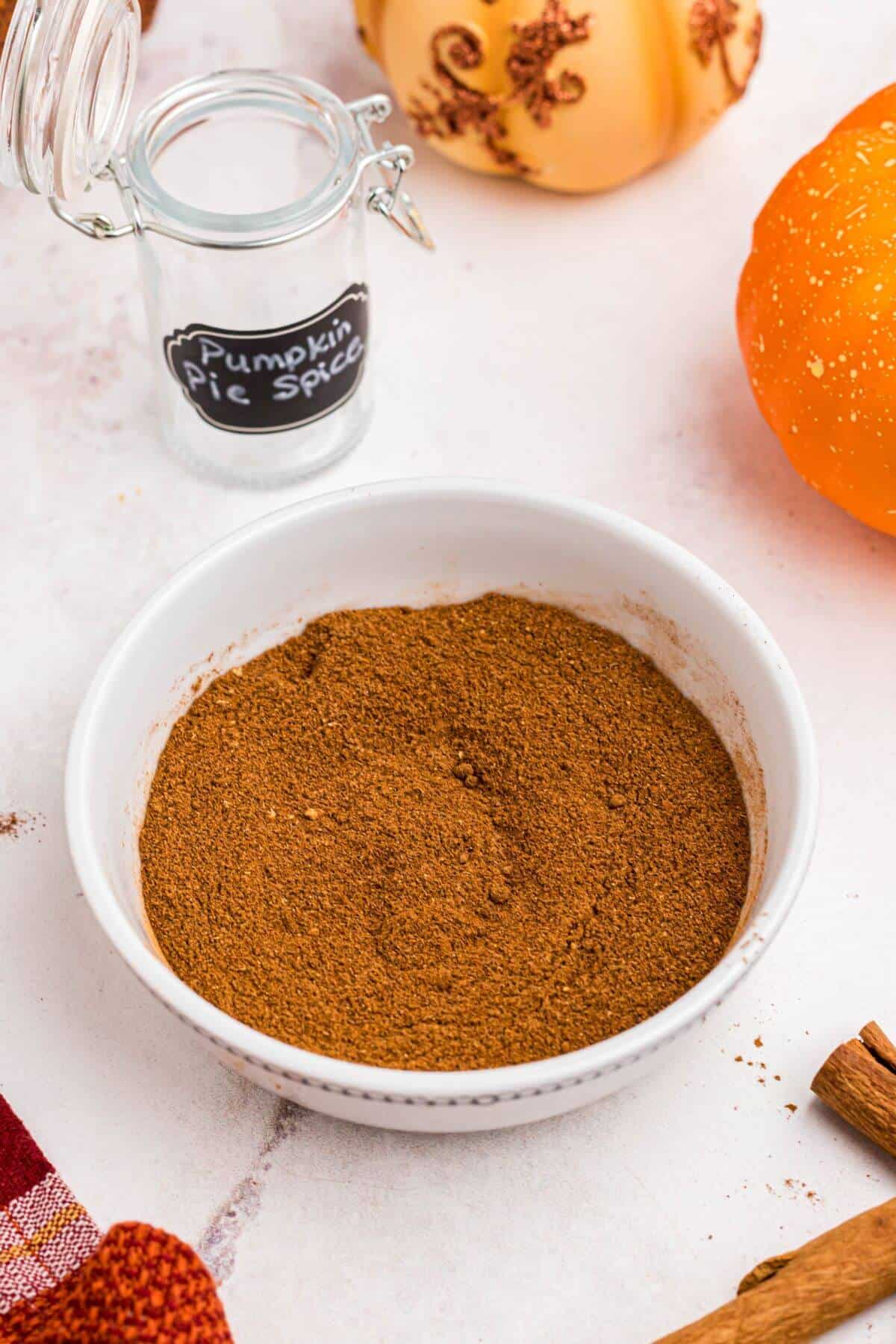 Pumpkin pie spice mixed and in a small white bowl in front of cinnamon sticks. 