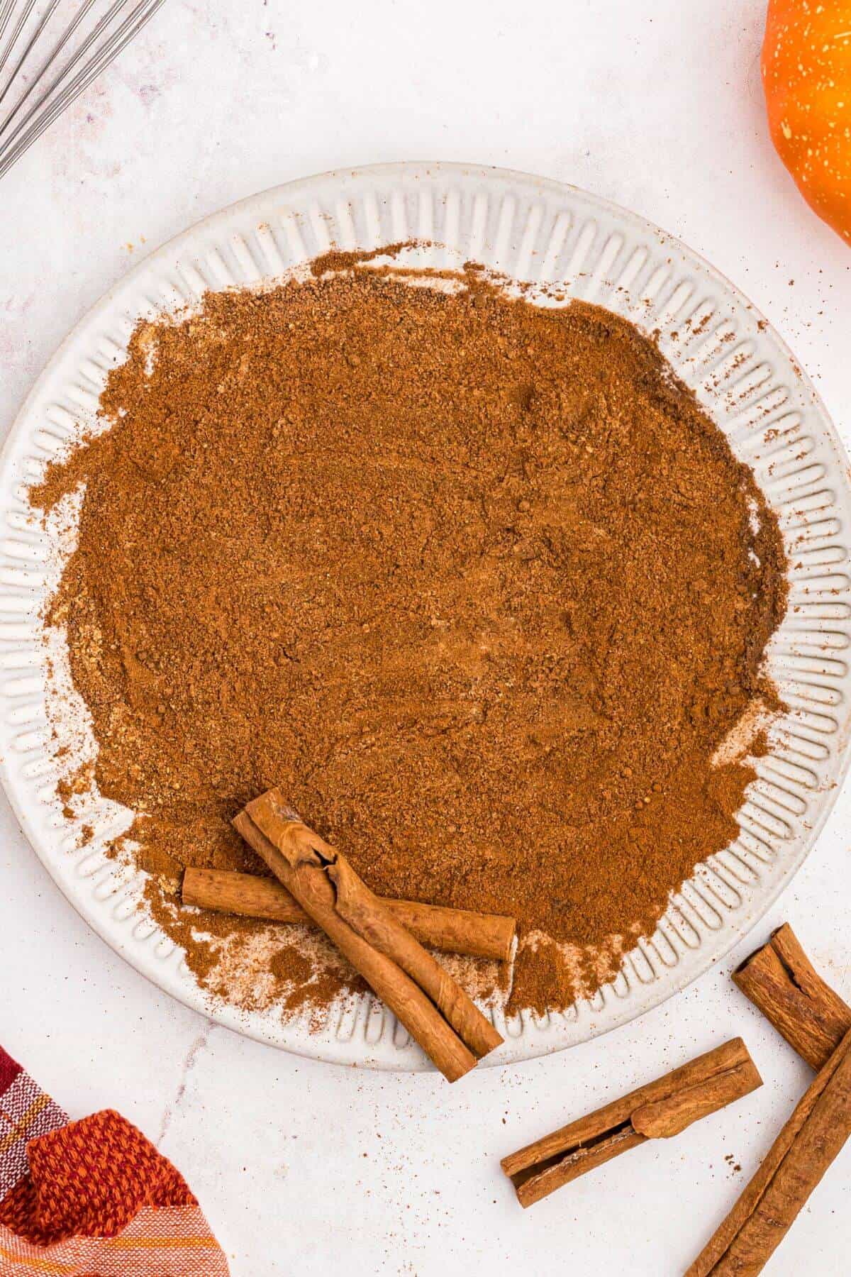 Spices mixed together on a white plate with cinnamon sticks. 