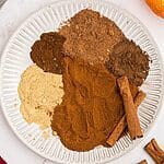 Spices measured out on a white plate to make pumpkin pie spice.