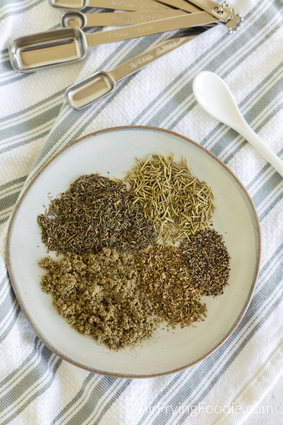 Seasonings needed to make poultry seasoning measured out and added to a plate. 