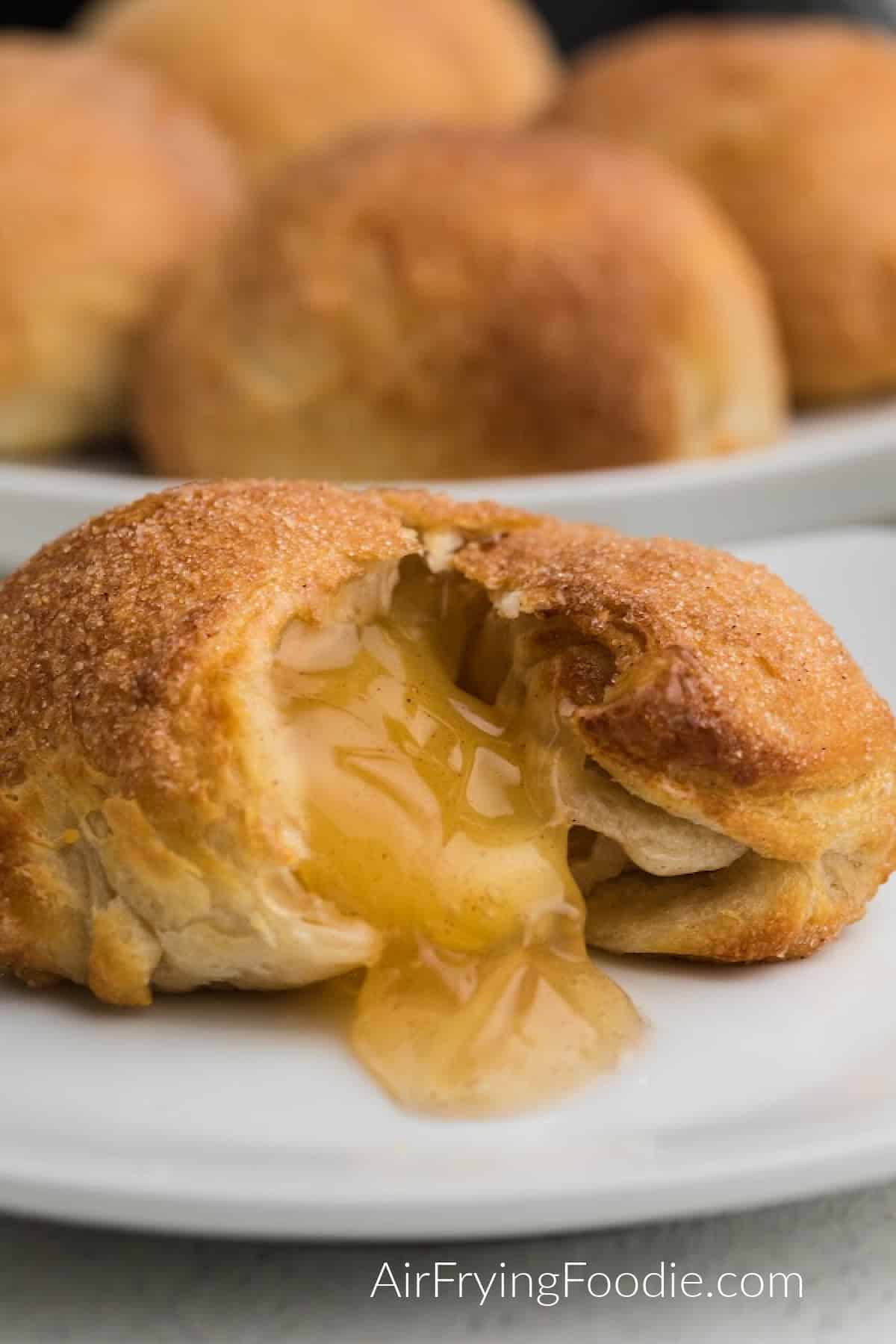 Close up of an air fryer apple pie bomb on a white plate, with apple and filling spilling out onto the plate. 