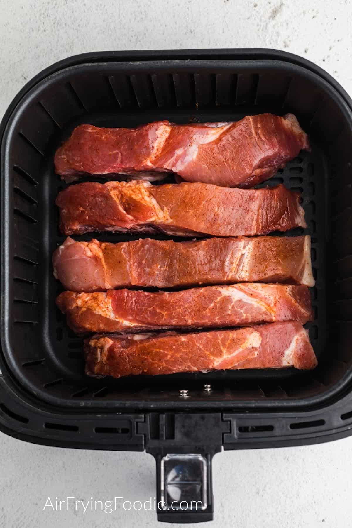 Seasoned country-style ribs in the basket of the air fryer, ready to cook. 