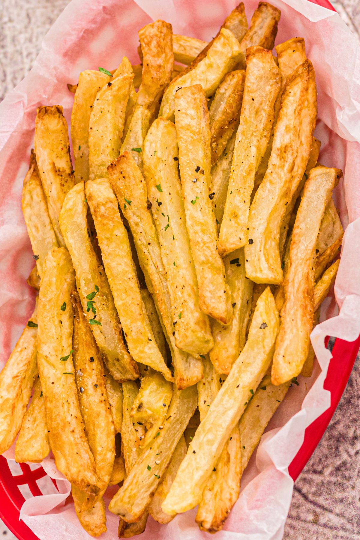 Golden French fries seasoned with salt in a red basket. 