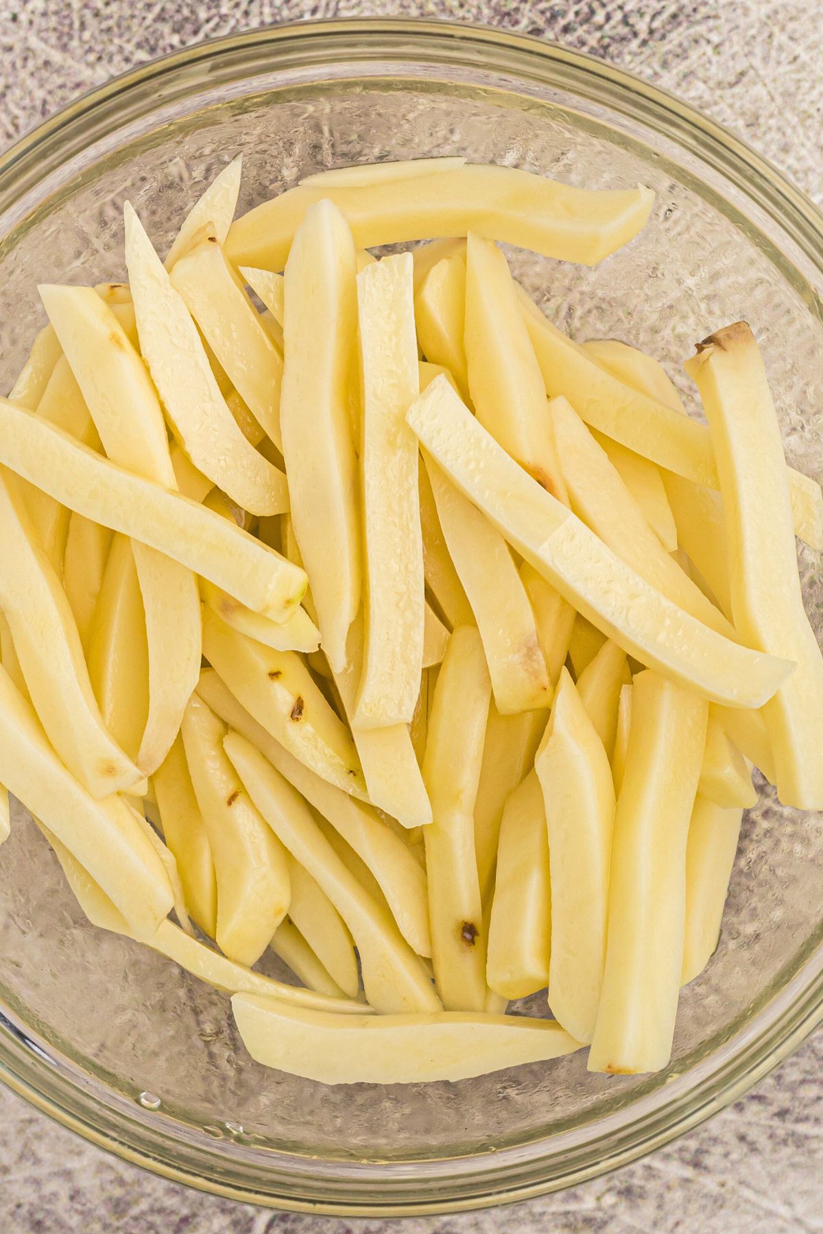 Potato slices cut and rinsed in a clear glass bowl. 