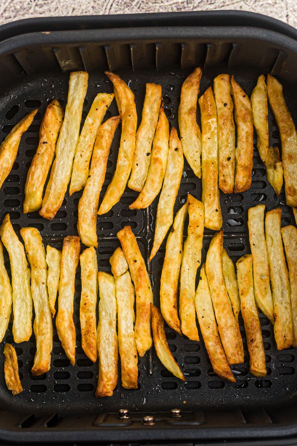 Golden French fries in an air fryer basket after being seasoned and air fried. 