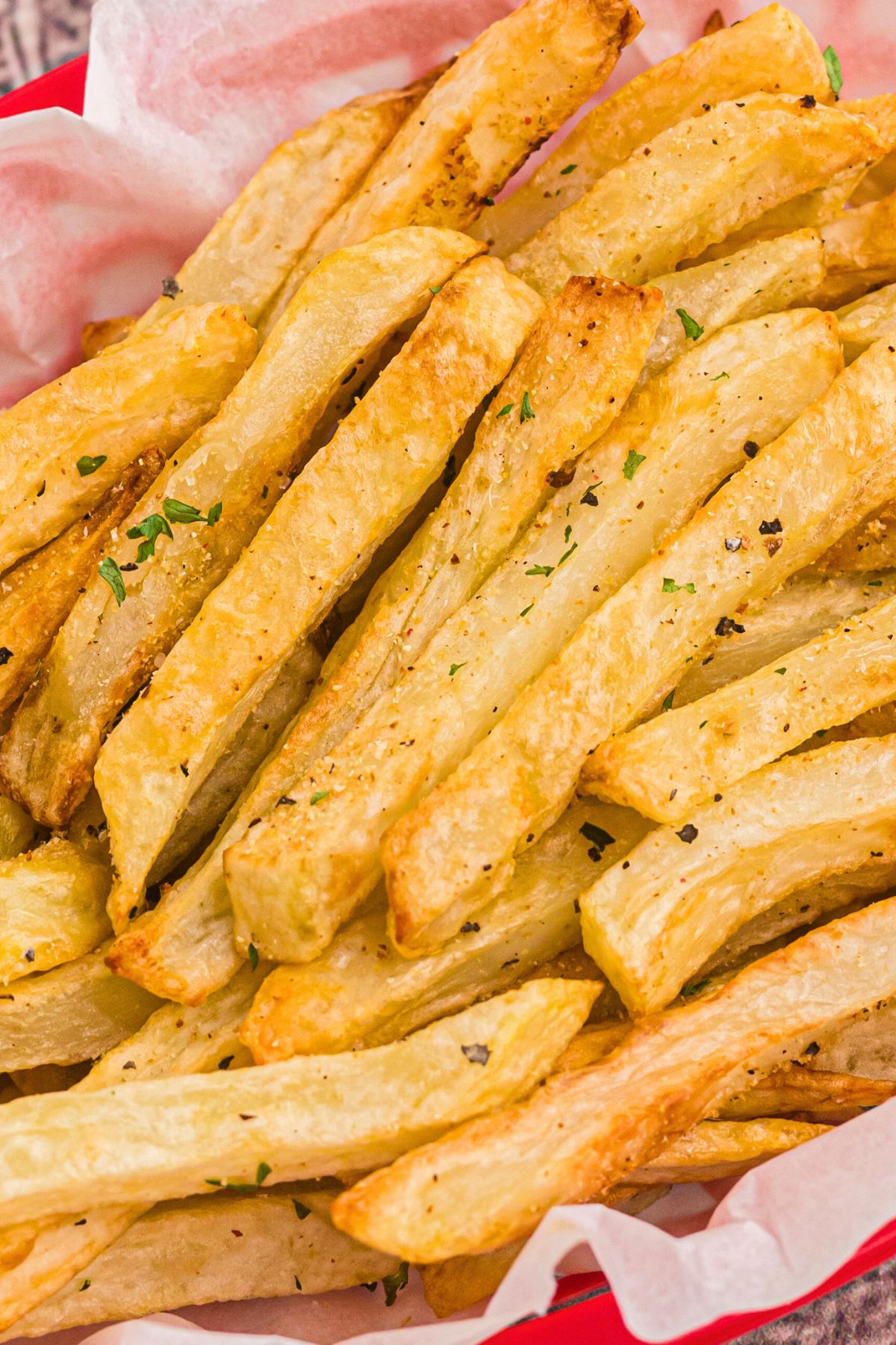 Up close photo of French fries seasoned with salt and garnished with small parsley flakes. 