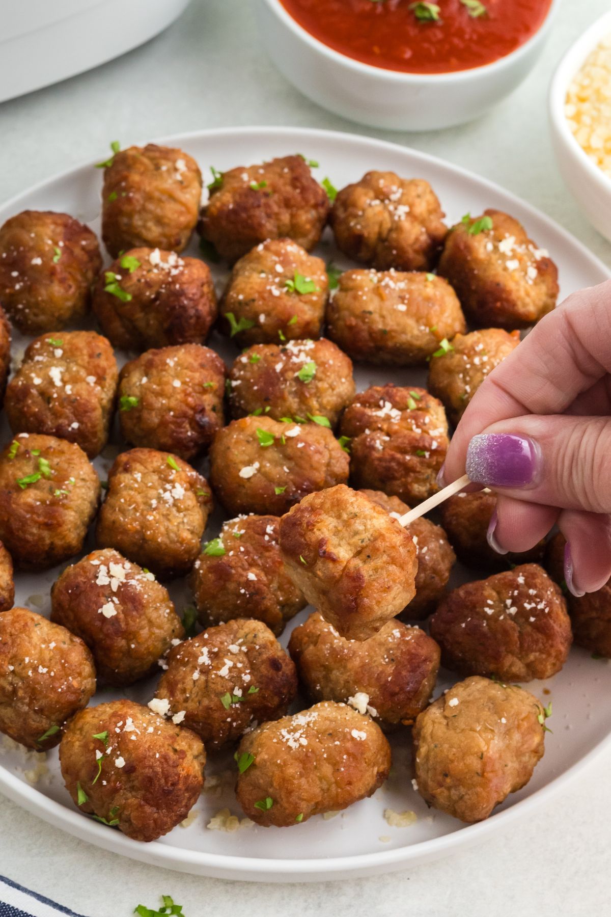 Juicy golden brown meatballs on a white plate skewered with a toothpick. 