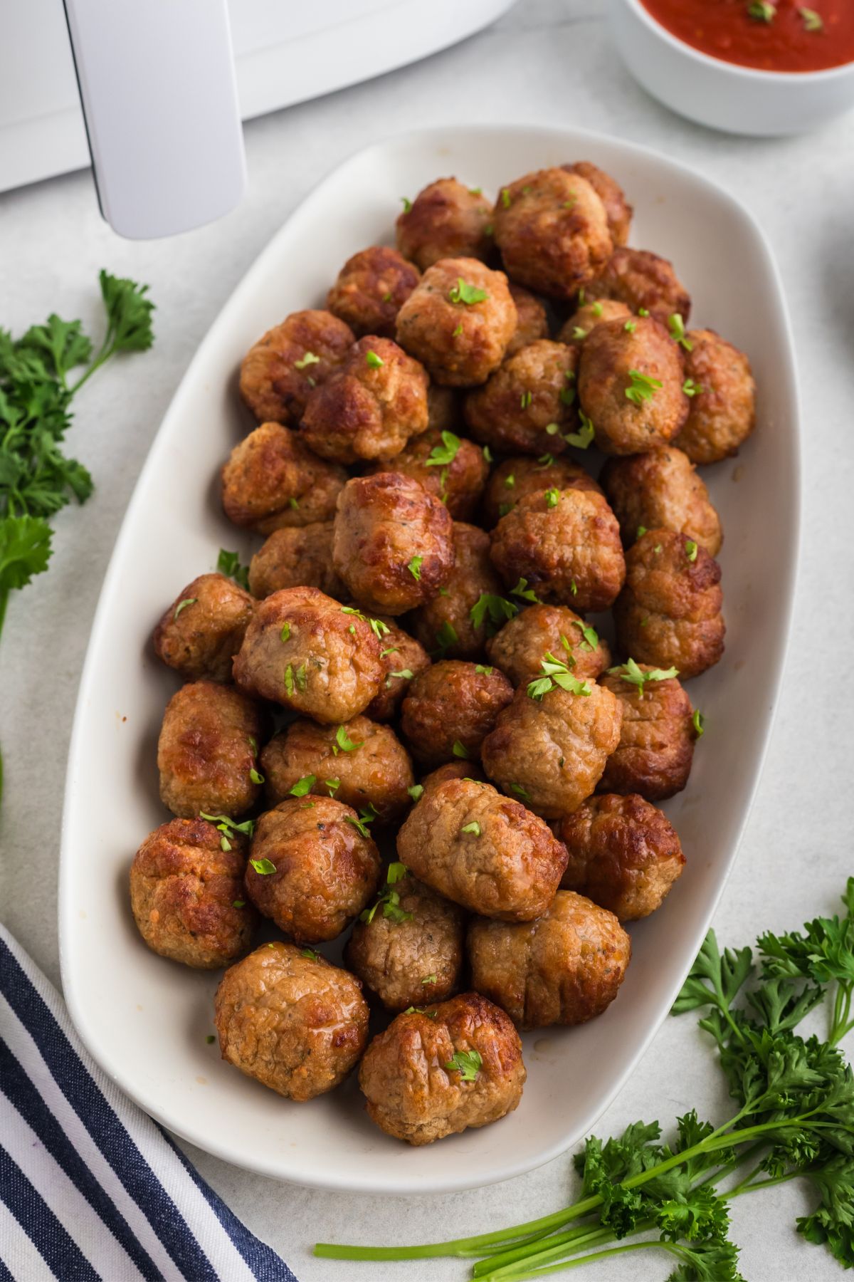 Juicy golden brown meatballs stacked on a white plate in front of an air fryer after being cooked. 