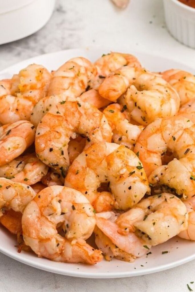 Orange garlic and butter shrimp stacked on a white plate. 