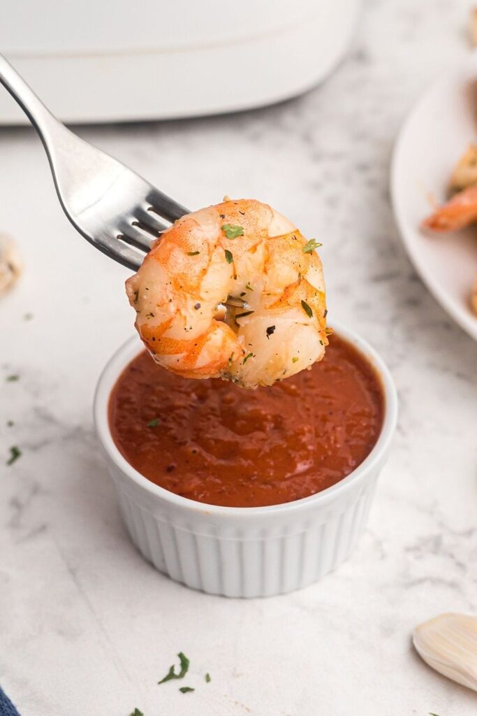 Orange seasoned shrimp being dipped into cocktail sauce. 