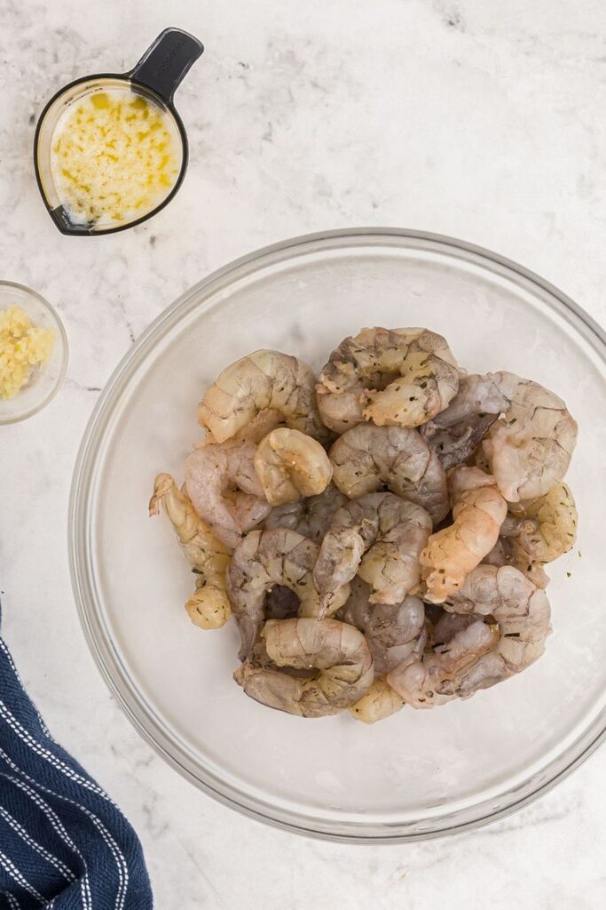 Uncooked shrimp, garlic, and melted butter on a marble table. 