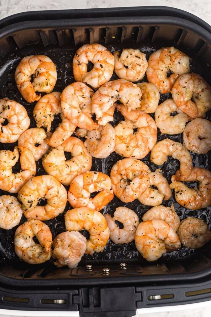 Cooked and orange golden color, shrimp tin the air fryer basket, coated with butter and garlic