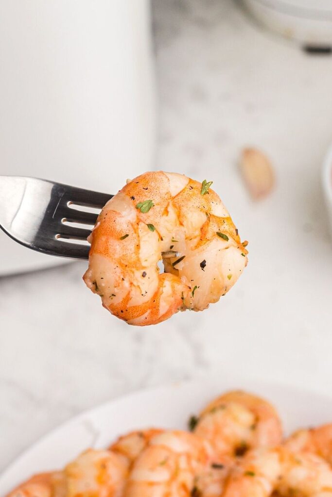 Close up bite shot of shrimp on a fork, seasoned and garnish with parsley flakes. 