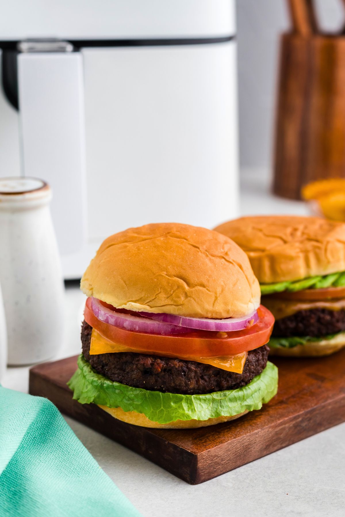 Impossible burger in a bun with traditional burger toppings in front of an air fryer. 