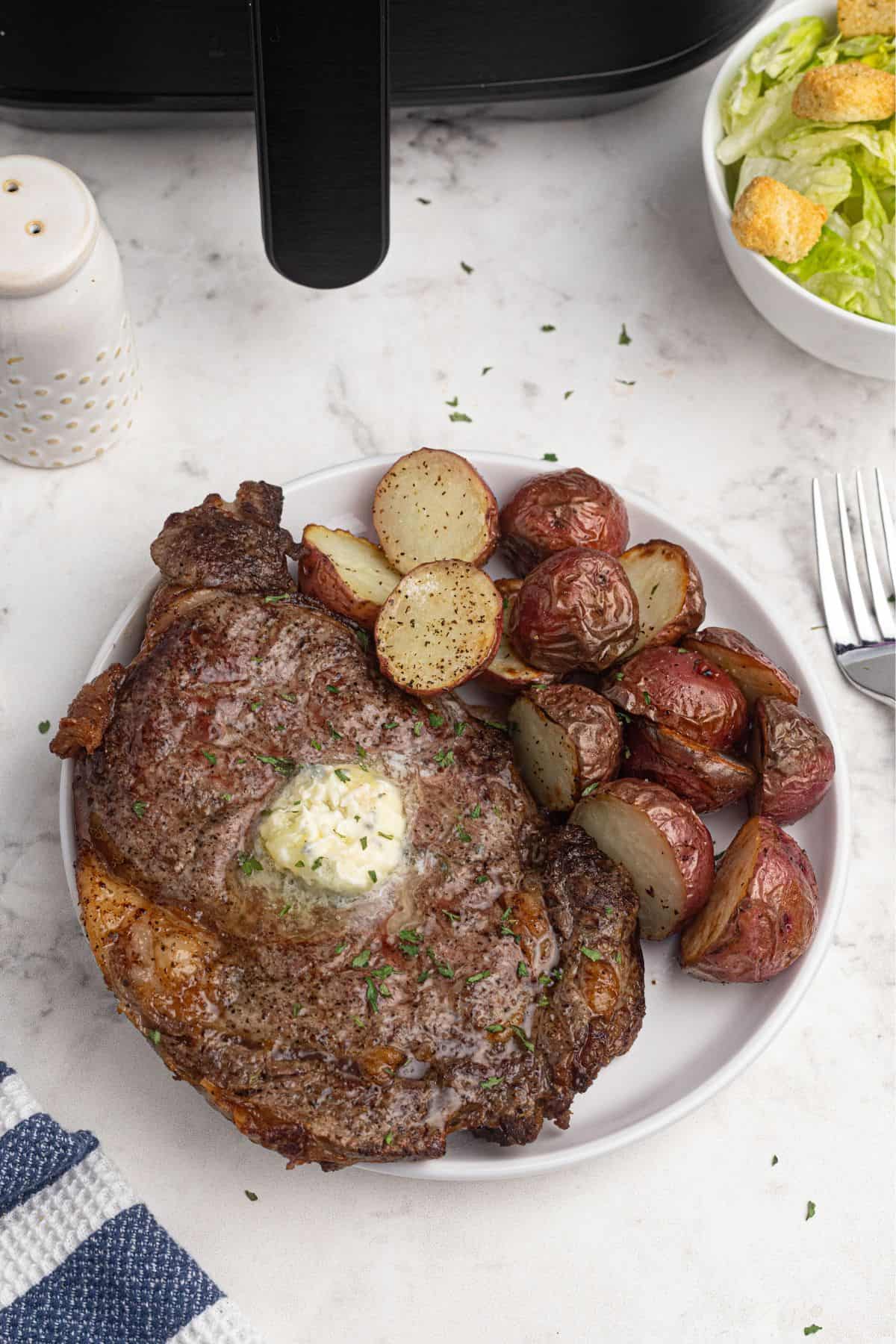 Juicy ribeye steak on a white plate with baby potatoes.