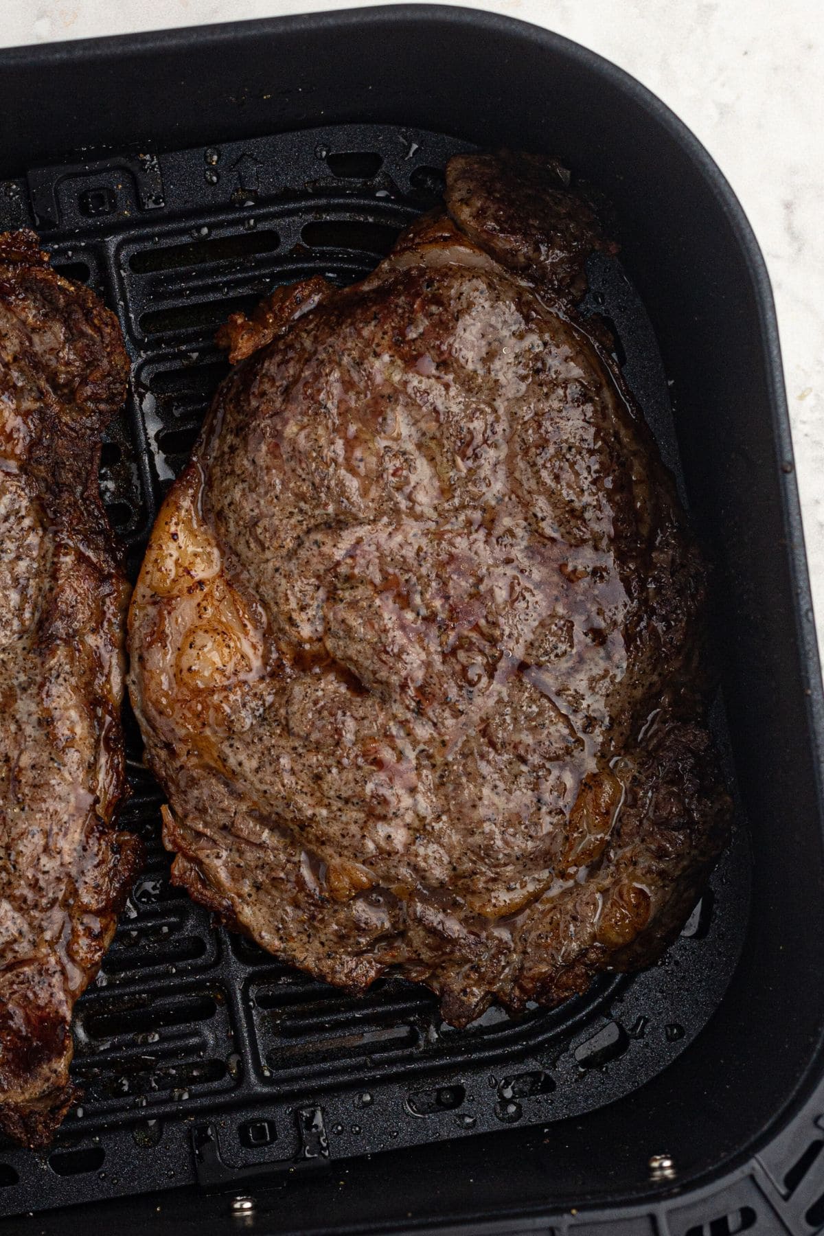 Close up picture of a juicy, seasoned ribeye steak in the air fryer basket. 