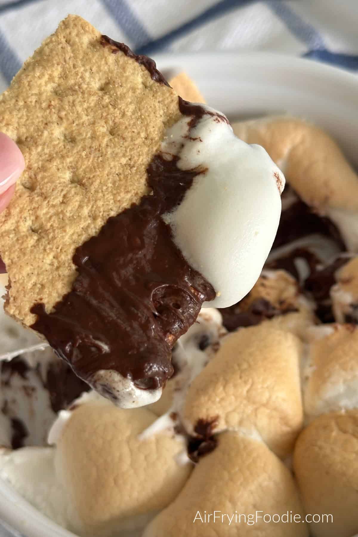 A close up of a graham cracker being dipped into the s'mores dip. 