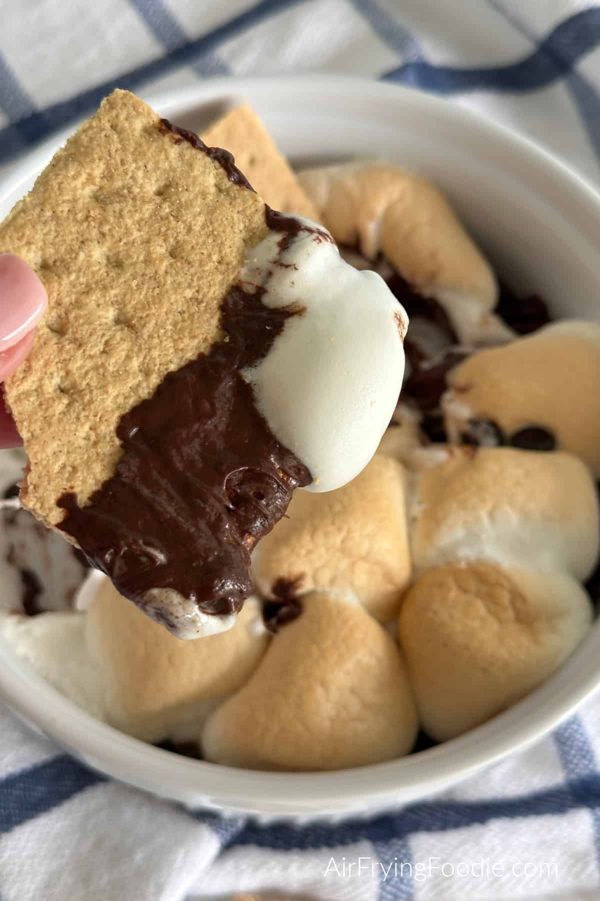 Graham cracker being dipped into S'more Dip that was made in a glass dish in the air fryer. 