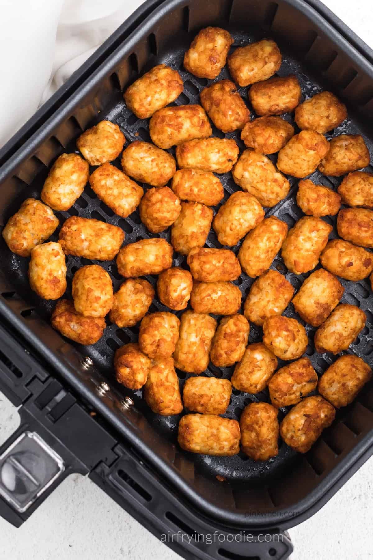 Tater tots fully cooked in the basket of the air fryer. 