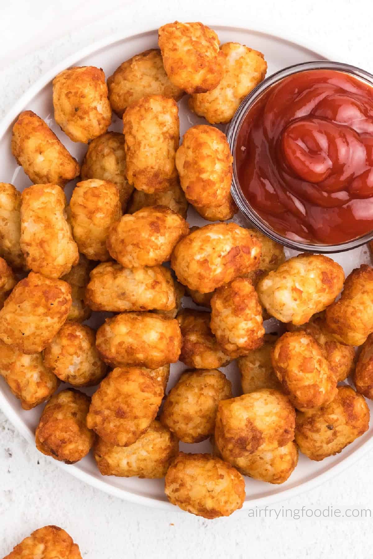 Tater tots made in the air fryer, served on a white plate with a side of ketchup. 